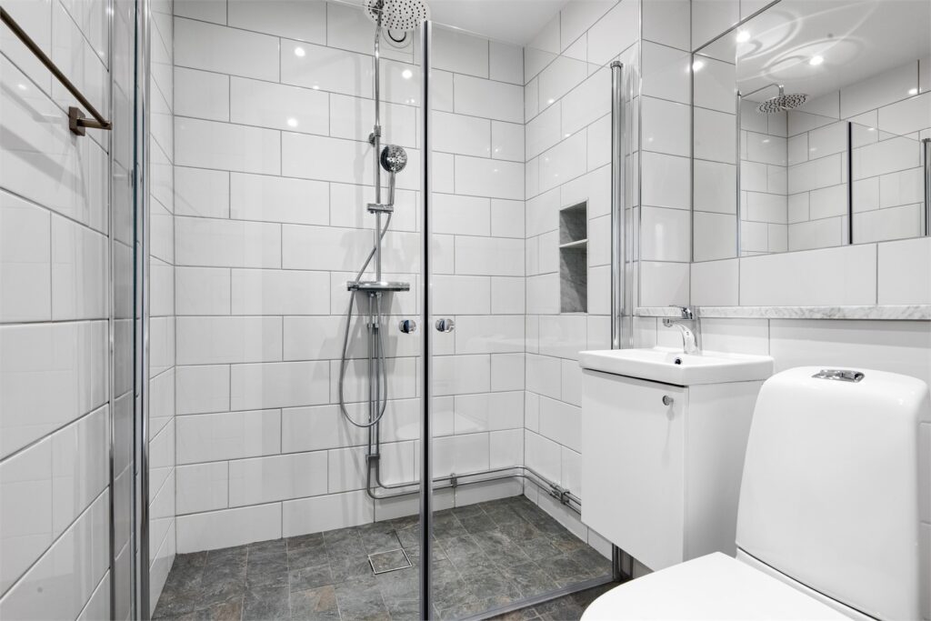 Badrumsrenovering i Fruängen med vitt kakel och mörkgrå klinker