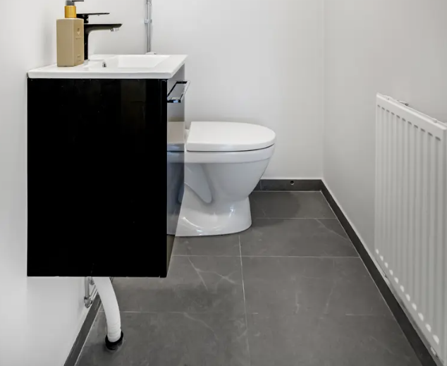 Renoverad WC med grå klinker och mörk kommod